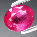 Oval red ruby gemstone with purplish background, held in silver tongs, certificate number 0.85ct.