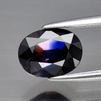 AIGS certificate 1.32ct VS oval purple blue sapphire with black facets, held in silver tweezers against a gray background.