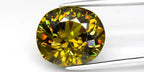 Large oval yellowish green demantoid garnet gemstone with rainbow-like reflections and inclusions, held by a silver-tone pick.