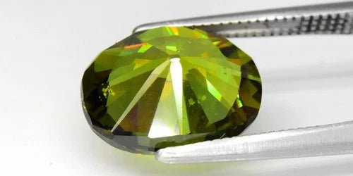 Large oval green demantoid gemstone with sharp facets, held by a silver-tone metal clamp against a white background.