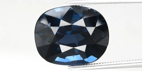 Large oval dark blue spinel with black centers and faceted triangular arrangement, viewed under white background.