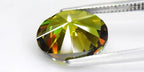 4.56ct VS oval brilliant natural yellowish green demantoid garnet gemstone with smooth edges, held in silver tongs.